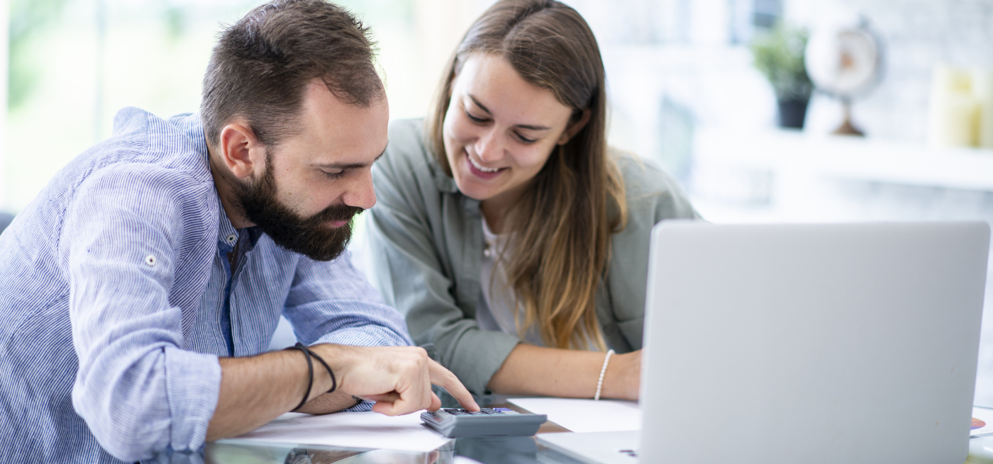 Casal a calcular valores com uma calculadora e portátil sobre a mesa